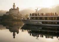 Elegant river cruise ship passing Marksburg Castle on the Rhine at golden hour